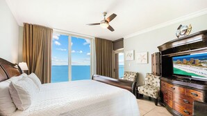 Habitación de hotel con una cama grande, ventilador de techo, televisión, escritorio y vista al océano.