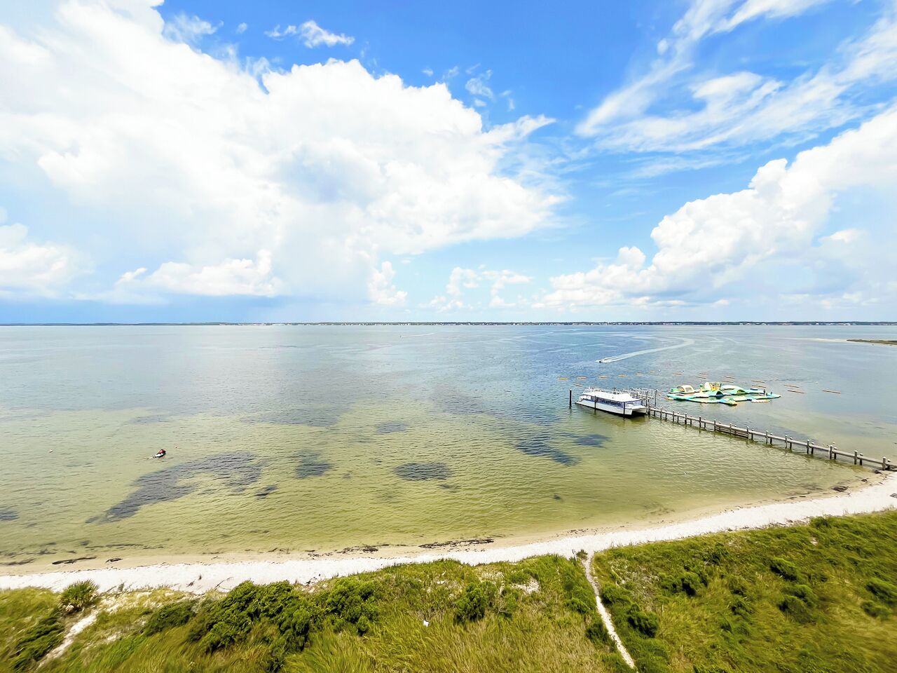 Een kustlandschap met een heldere lucht, een zandstrand en een pier die in het water uitloopt.