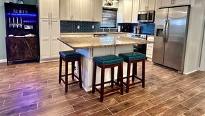 Una cocina moderna con armarios blancos, un refrigerador de acero inoxidable y una barra con taburetes.