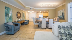 A spacious living room with a dining area, a kitchen in the background, and artwork on the walls.