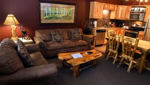A cozy living room with a brown sofa, a wooden coffee table, and a dining area with a rustic wooden table and chairs. - Newly remodeled 2 bedroom, 2 bath condo with mountain and river views (Estes Park)