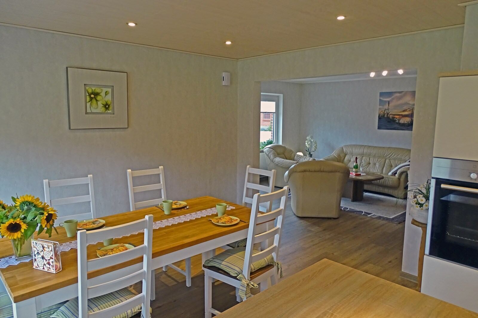 A dining area with a wooden table and white chairs, a sofa, and a kitchen area with a stove.