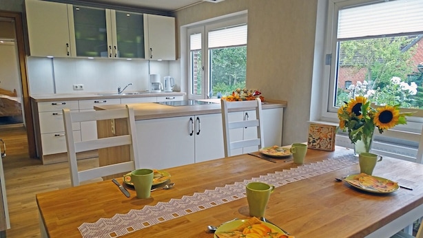 A modern kitchen with white cabinets, a wooden countertop, and a dining area with a wooden table set for two. - "Mee(h)r" Vacation Rental in Olpenitz (Hasselberg)