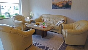 A living room with a beige leather sofa, two armchairs, a coffee table, and a painting on the wall. - "Mee(h)r" Vacation Rental in Olpenitz (Hasselberg)