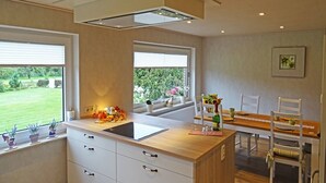 A modern kitchen with a central island, a dining area with a wooden table and chairs, and large windows offering a view of a garden. - "Mee(h)r" Vacation Rental in Olpenitz (Hasselberg)