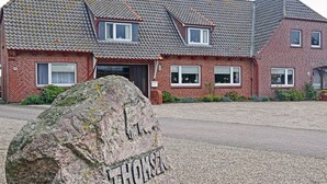 A red brick building with a tiled roof and multiple windows. A large rock with the inscription "Thomsen" is in the foreground. - "Mee(h)r" Vacation Rental in Olpenitz (Hasselberg)