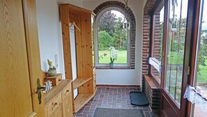 A wooden cabinet with drawers, a hanging coat rack, a small table with a vase, and a view of a garden through a window. - "Mee(h)r" Vacation Rental in Olpenitz (Hasselberg)