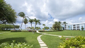 A well-maintained garden with a winding path, palm trees, and a building with a light blue facade.