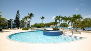 A pool area with lounge chairs and palm trees, surrounded by a building with balconies.