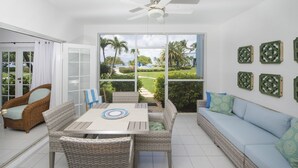 A spacious patio with a dining table, wicker furniture, and a view of a lush garden.
