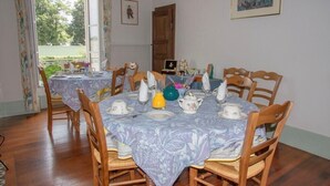 Uma sala de jantar com uma mesa posta para quatro pessoas, cadeiras de madeira e toalha de mesa florida.