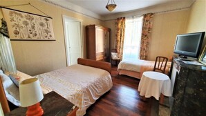 Quarto de hotel com duas camas, uma mesa de trabalho com televisão, um guarda-roupa e um quadro na parede.