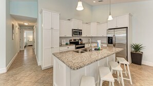 A modern kitchen with white cabinetry, granite countertops, stainless steel appliances, and a central island with bar stools.