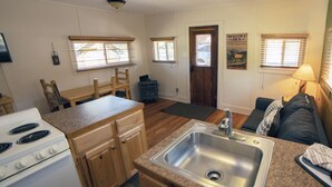 Une cuisine compacte comprenant un évier, une cuisinière, des placards en bois et un coin repas avec une table et des chaises.