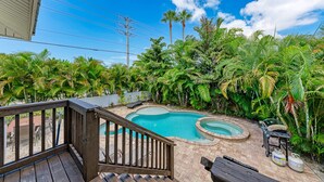 Un patio trasero con piscina, terraza de madera y exuberante vegetación tropical.
