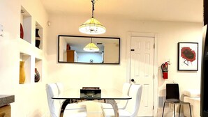 A dining area with a glass table and white chairs, a yellow hanging light fixture, a white door, and a fire extinguisher mounted on the wall.