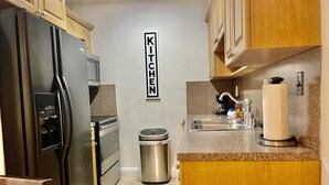 A compact kitchen with a stainless steel refrigerator, a microwave, a sink, and a trash bin.