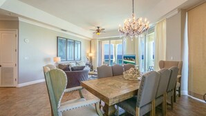 A spacious dining area with a wooden table and chairs, a chandelier, and a view of the ocean through large windows.