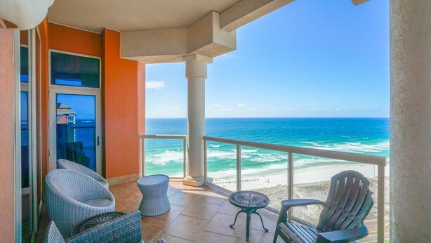 A balcony with wicker chairs, a small round table, and a view of the ocean.