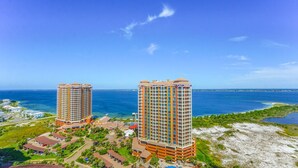 Two high-rise hotels with balconies, located near a beach with clear blue waters and a small island in the distance.