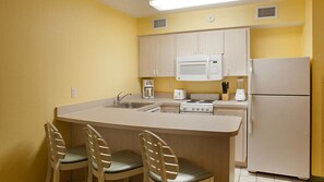 A compact kitchen with a central island, a microwave, a stove, a refrigerator, and two bar stools.