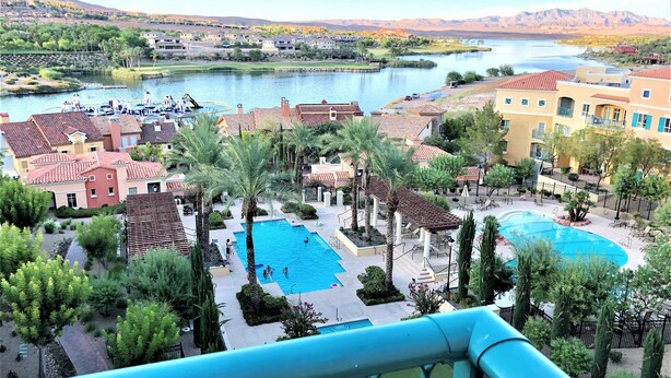 A resort with multiple swimming pools, palm trees, and a view of a lake and mountains. - Top floor, BEST view, Viera condo at Lake Las Vegas! (Henderson)