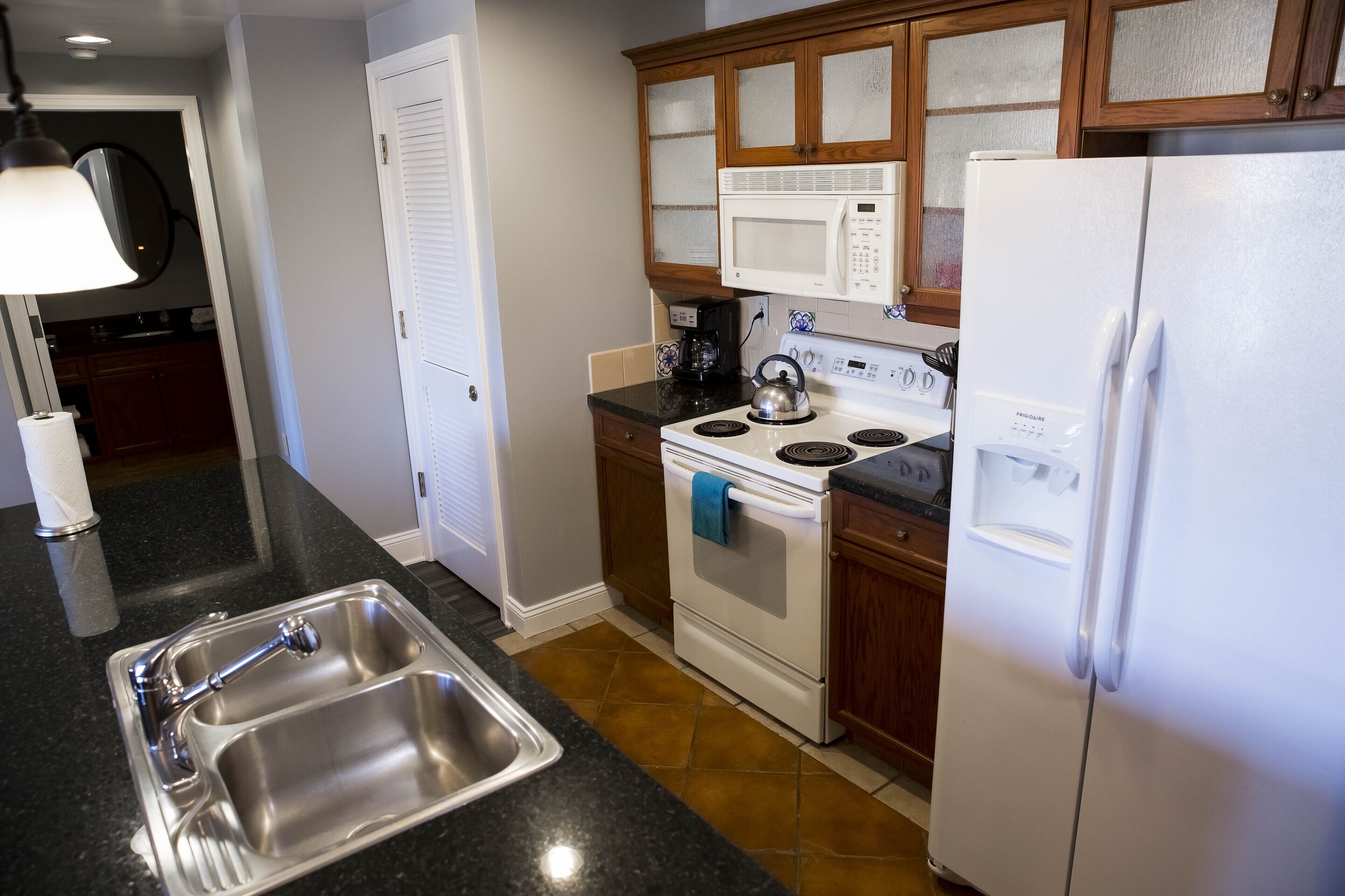 Una cocina con un lavamanos de acero inoxidable, una estufa, un microondas y un refrigerador.