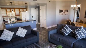 A modern living room with two dark sofas, a glass coffee table, and a dining area with a wooden table and chairs. - Top floor, BEST view, Viera condo at Lake Las Vegas! (Henderson)