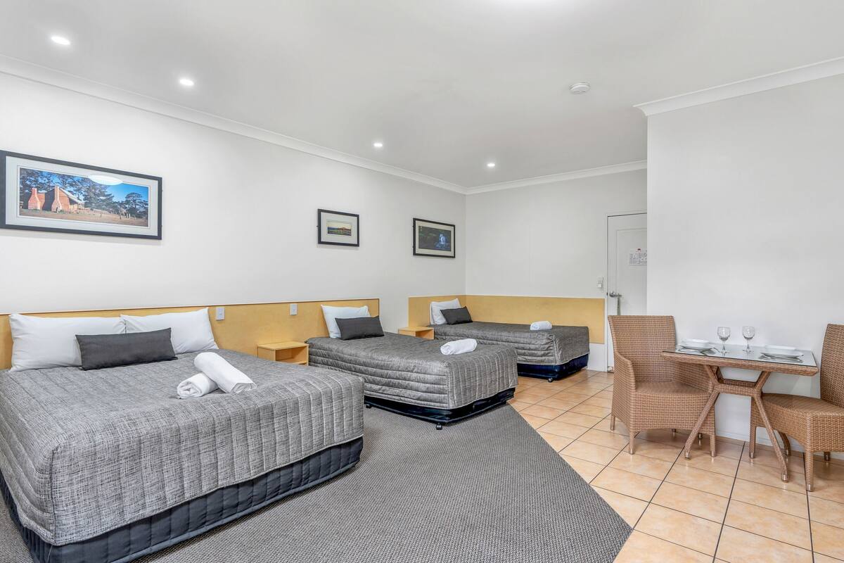Ein Hotelzimmer mit zwei Betten, einem Esstisch mit Stühlen und einem kleinen Balkon.