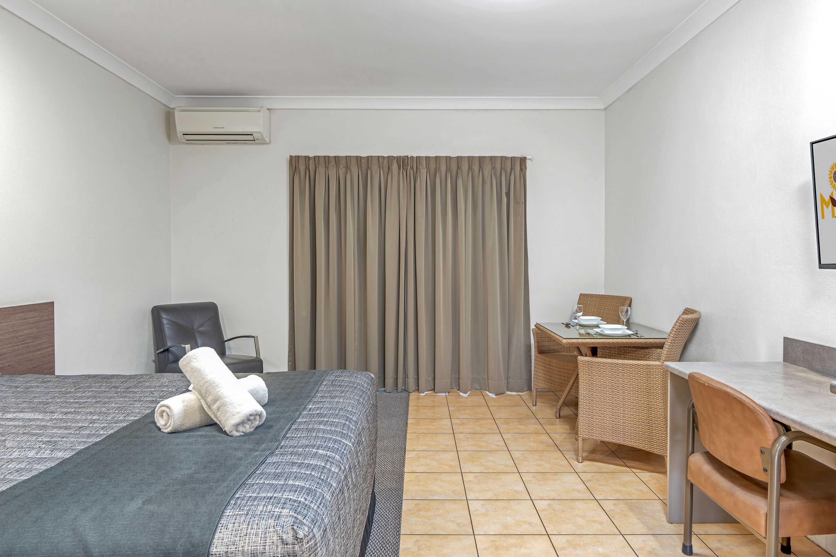 Een hotelkamer met twee bedden, een eettafel met stoelen, een bijzettafeltje met een stoel en een airconditioner.