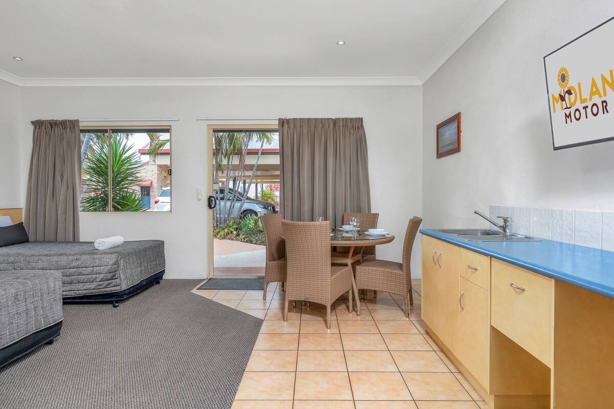 Ein Hotelzimmer mit Bett, Esstisch mit Stühlen, einer Küchenzeile und Blick ins Freie.