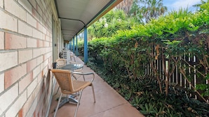 A covered outdoor seating area with brick walls, metal chairs, and a concrete floor. - Midlander Motor Inn (Emerald)