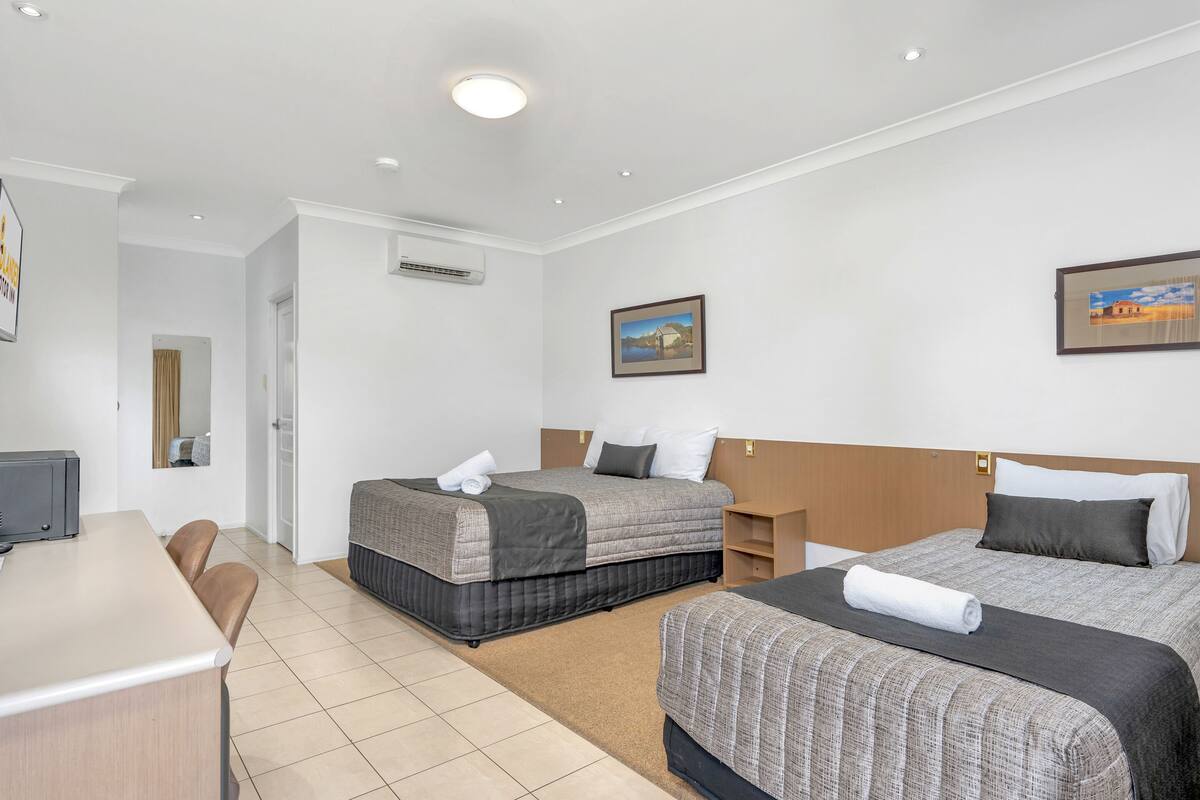 Ein Hotelzimmer mit zwei Betten, einem Schreibtisch, Stühlen und einem Bild an der Wand.