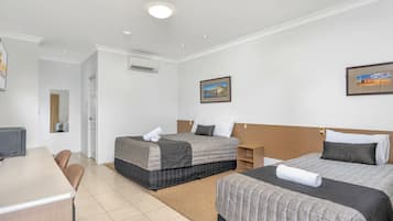 A hotel room with two beds, a desk, chairs, and a painting on the wall.