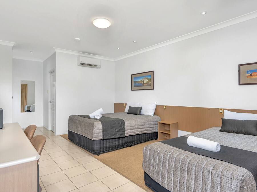 A hotel room with two beds, a desk, chairs, and a painting on the wall.