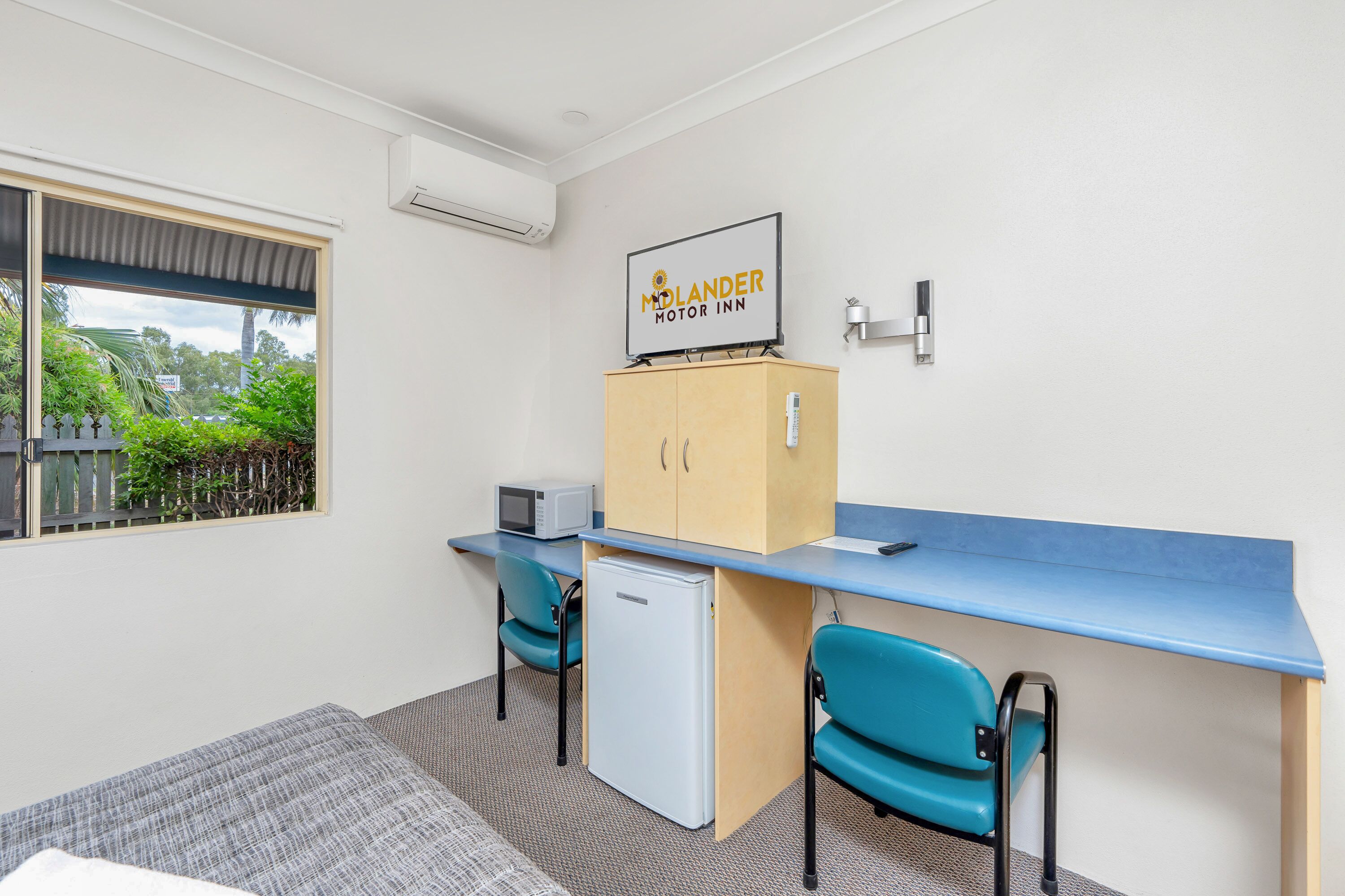 A compact room with a blue desk, two teal chairs, a small white refrigerator, and a microwave. A sign reads "MOLANDER MOTOR INN."