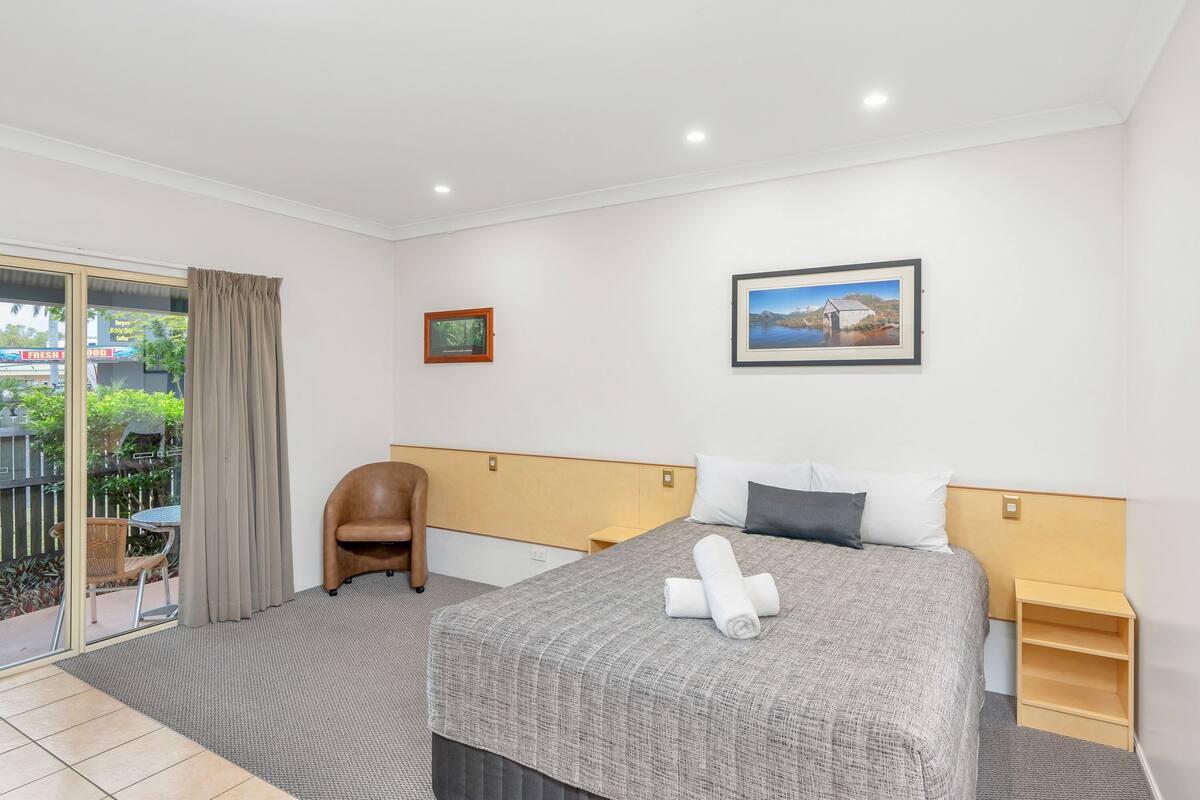 Ein Hotelzimmer mit Bett, Stuhl, kleinem Tisch und Blick ins Freie.