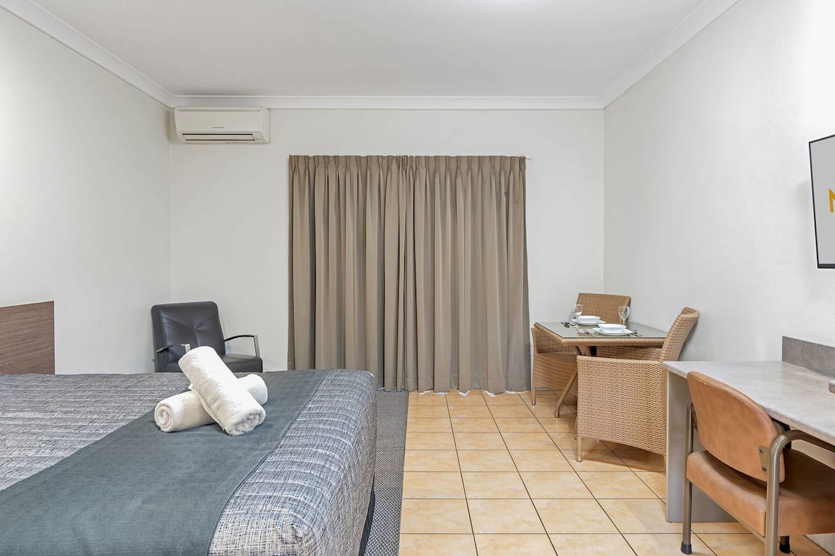Quarto de hotel com cama, poltrona, mesa pequena com cadeira e escrivaninha.