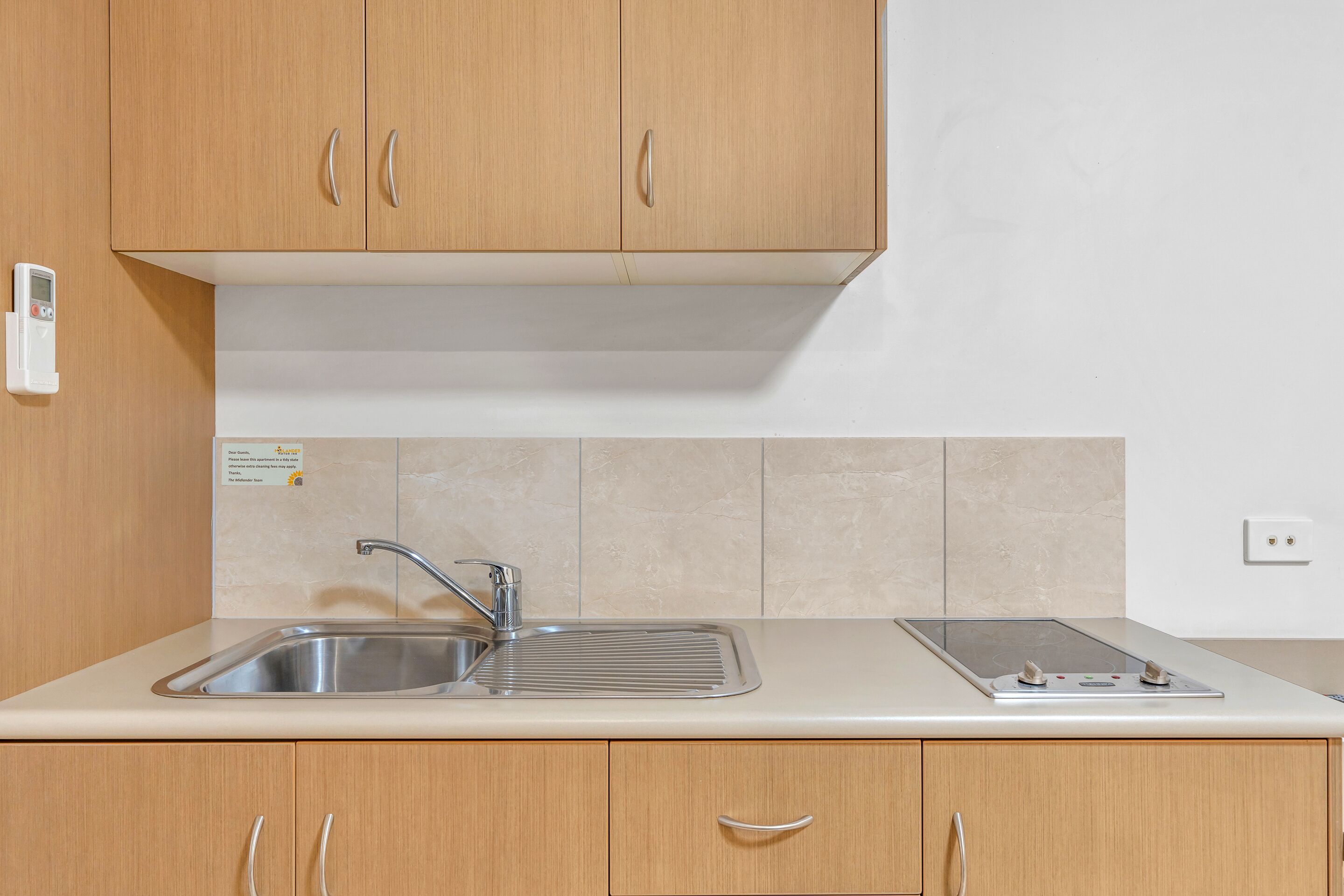 A kitchen with wooden cabinets, a stainless steel sink, a built-in stove, and a wall-mounted electrical outlet.