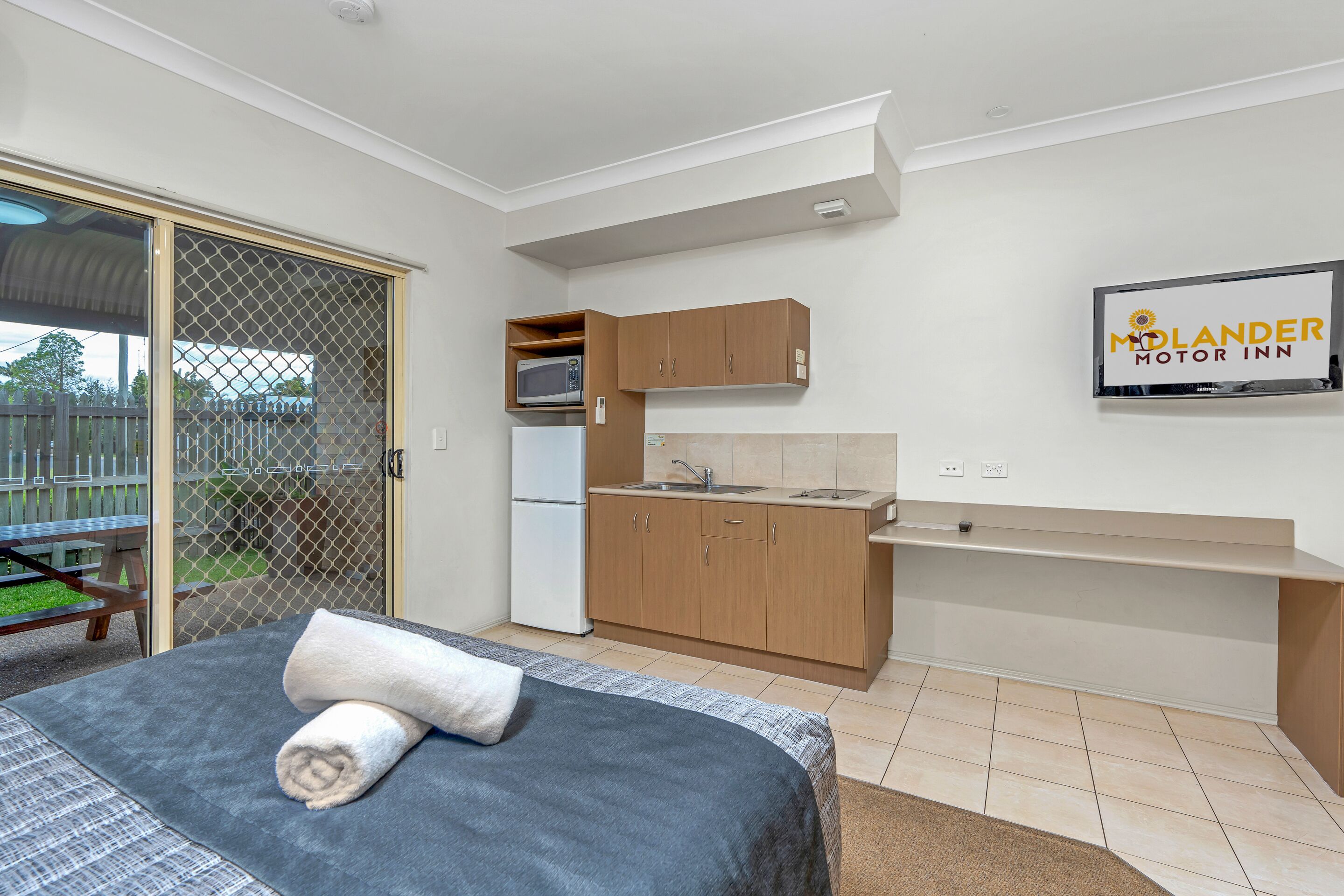 Une chambre d’hôtel compacte comprenant un lit, une petite kitchenette et une porte-fenêtre coulissante donnant sur un espace extérieur.