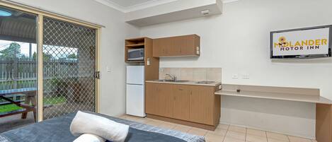 Une chambre d’hôtel compacte comprenant un lit, une petite kitchenette et une porte-fenêtre coulissante donnant sur un espace extérieur.