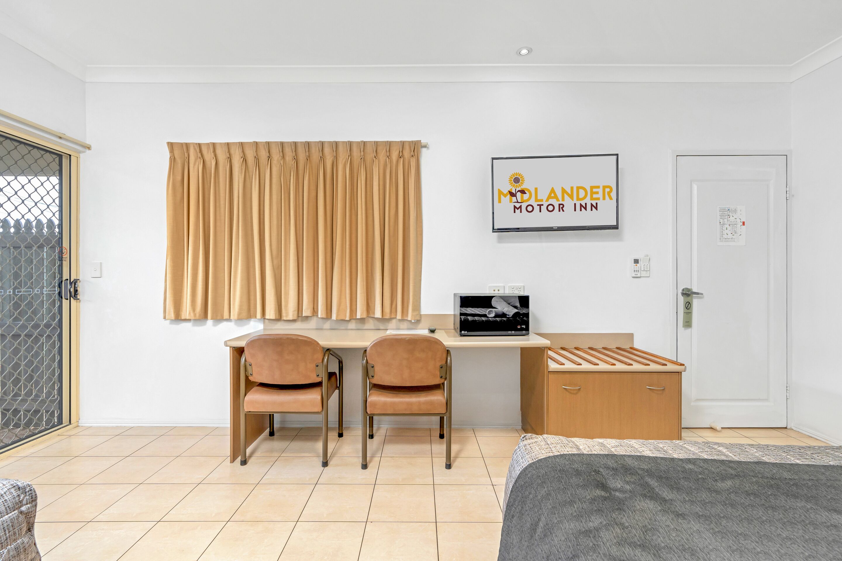 A hotel room with a bed, a desk with two chairs, a TV, and a sign for 'MOLANDER MOTOR INN'.