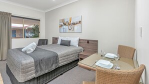 A hotel room with a bed, a dining table, and a painting on the wall. - Midlander Motor Inn (Emerald)