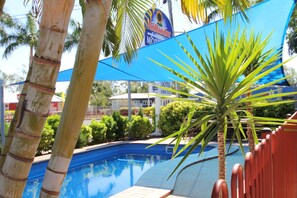 A swimming pool surrounded by palm trees and a blue shade sail.