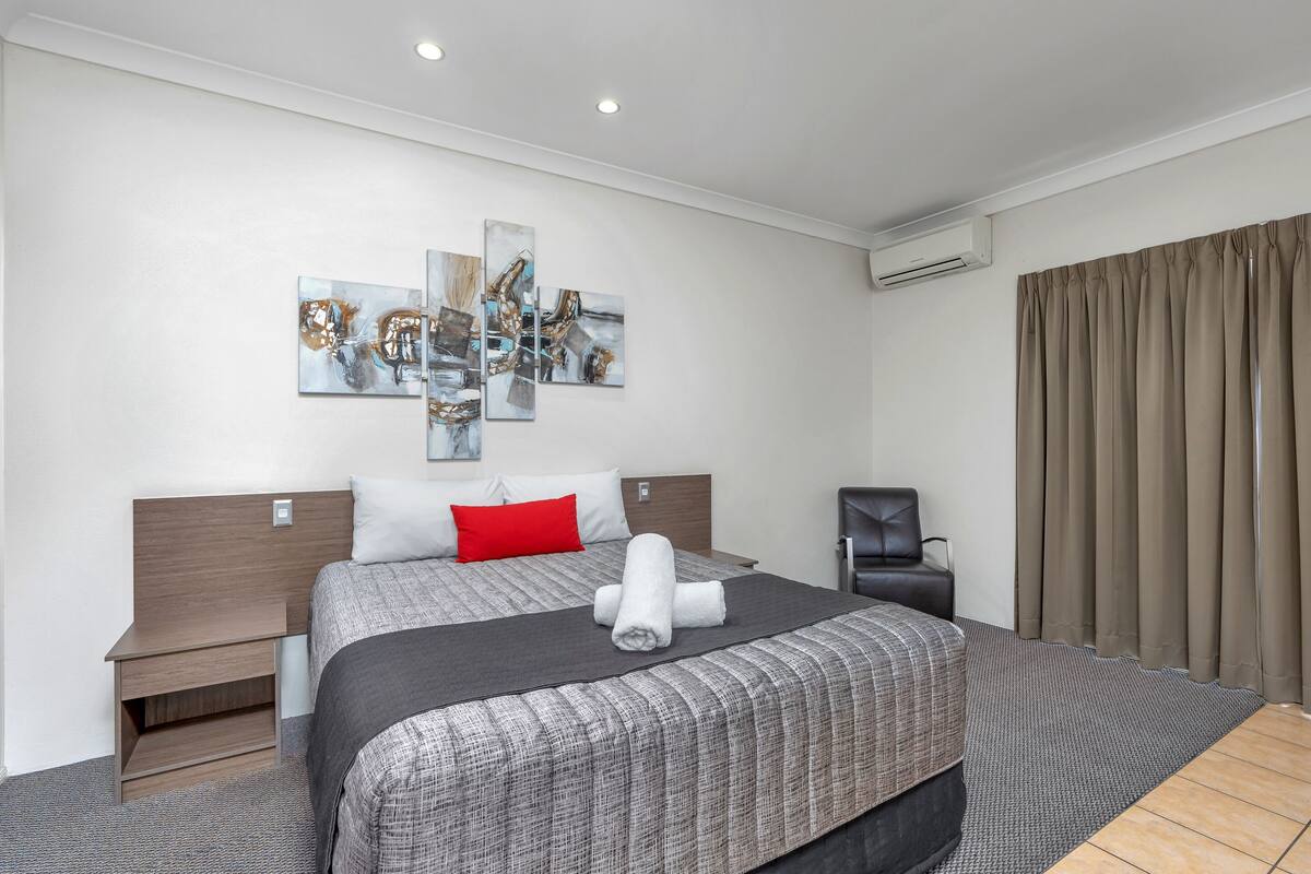 Ein modernes Hotelzimmer mit einem großen Bett, einem Nachttisch, einem Sessel und Kunstwerken an der Wand.