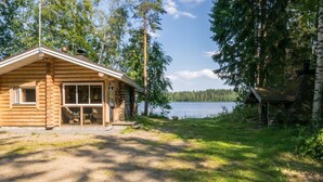 A log cabin with a large window and a door, a porch with a chair, and a view of a lake. - Lemmenmaja by Interhome (Juva)