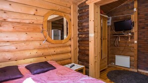 A wooden cabin room with a bed, a mirror, a television, and a small kitchenette. - Lemmenmaja by Interhome (Juva)