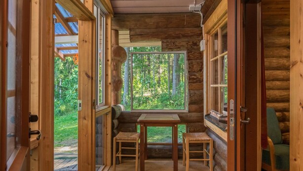 A log cabin with a wooden table and two chairs, large windows, and a view of the forest. - Lemmenmaja by Interhome (Juva)