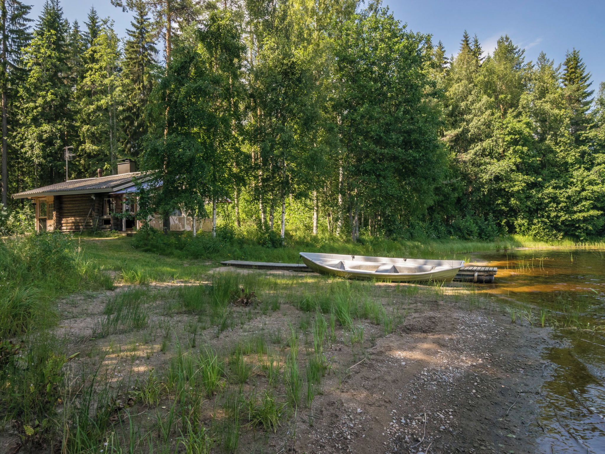 Une cabane avec un quai et un bateau, située sur la rive d’une rivière bordée d’une forêt.