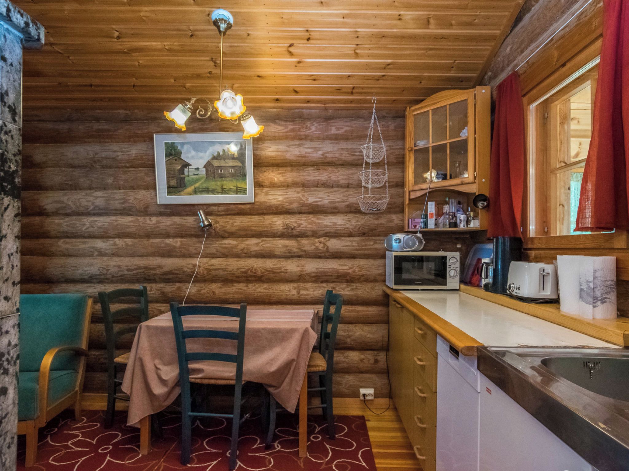 A wooden cabin interior with a dining table, chairs, a kitchen area with a microwave, and a hanging light fixture.